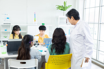 Asian students in science classroom engaged in experiments with beakers and laptop. Senior teacher supervising diverse group of young secondary pupils. Laboratory collaboration. back-to-school concept