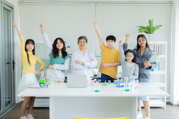 Group of students and senior teacher in science classroom waving arms happy learning in private...
