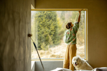 Young woman paints walls while making repairment of a new house. Creative process of home...