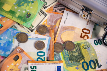 Close-up view of various Euro banknotes and coins, with a US dollar bill peeking out, scattered on...