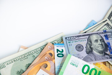 Close-up photo of US dollar and Euro bills piled haphazardly on white background. Denominations: 100/1 USD, 100/20 Euro