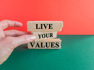 Concept words Live your values on brick blocks. Businessman hand. Beautiful red background, green table. Business, psychological and live your values concept.