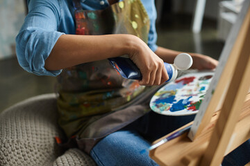 woman wearing an apron squeezes paint onto a palette in her art studio.
