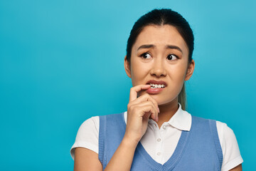 A young Asian woman in smart casual attire looks thoughtfully to the side, biting her lip as she considers her options.