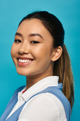 A young woman with a warm smile, dressed in smart casual attire, poses against a bright blue background.