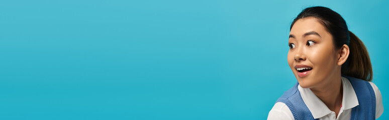 A young Asian woman in smart casual attire smiles and looks over her shoulder against a vibrant blue background.