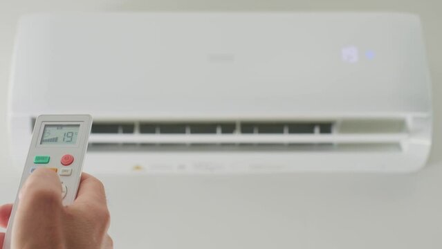 Adjusting air conditioner temperature with remote control. Hand holds remote control and setting comfortable temperature on climate system in apartment