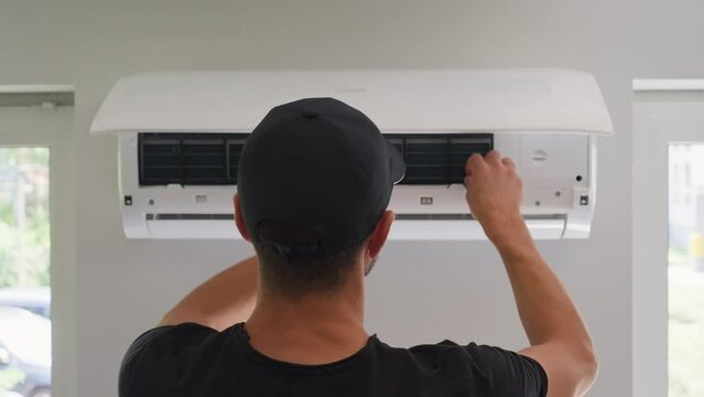 Air conditioner maintenance. Male technician repairs home climate system in living room. Man is cleaning filters of conditioner
