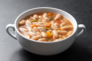 White beans soup with vegetables in white bowl on black background