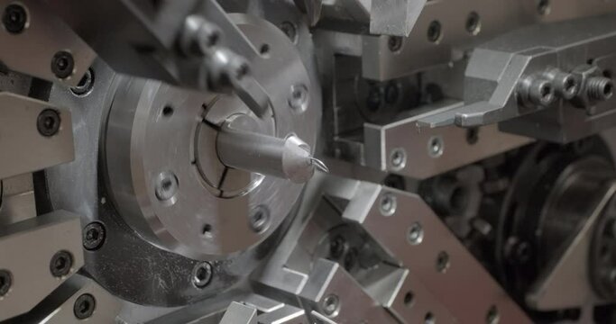 Automatic machine bends, twists and cuts wire, makes springs. Close up handheld shot, real time motion, artificial indoors light.