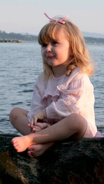 Little girl claps her hands sitting near the ocean sea river on a stone with a pink cake in a dress celebrate birthday joy happiness childish. The child points his finger to the side