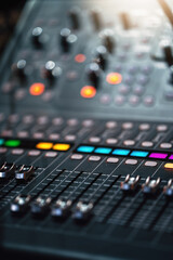 Close-up of professional audio mixing console with colorful illuminated buttons and sliders, used in music production and live performances. Modern sound equipment in recording studio.