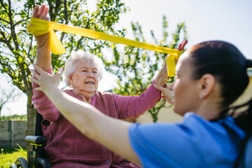 Female caregiver doing motorized exercises with senior woman in wheelchair. Nurse and elderly woman...