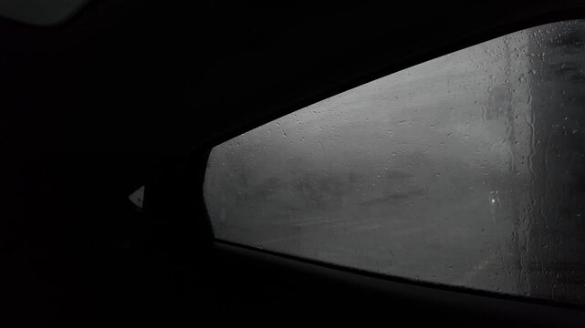View from inside dark car, condense fog on window, raining, cars passing