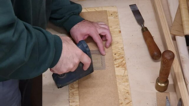 The carpenter uses an electric staple gun to attach a metal grid to the workpiece.