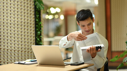 Concentrated businessman sitting at modern coworking space and working on laptop