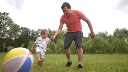Fototapeta premium Father and baby son playing ball in the park. Love countryside men concept. A father and child baby playing a ball in a park. Father and son playing ball in the park. happy fun childhood concept.