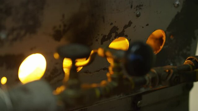 Worker's hand igniting coffee roasting machine and adjusting fire strength.