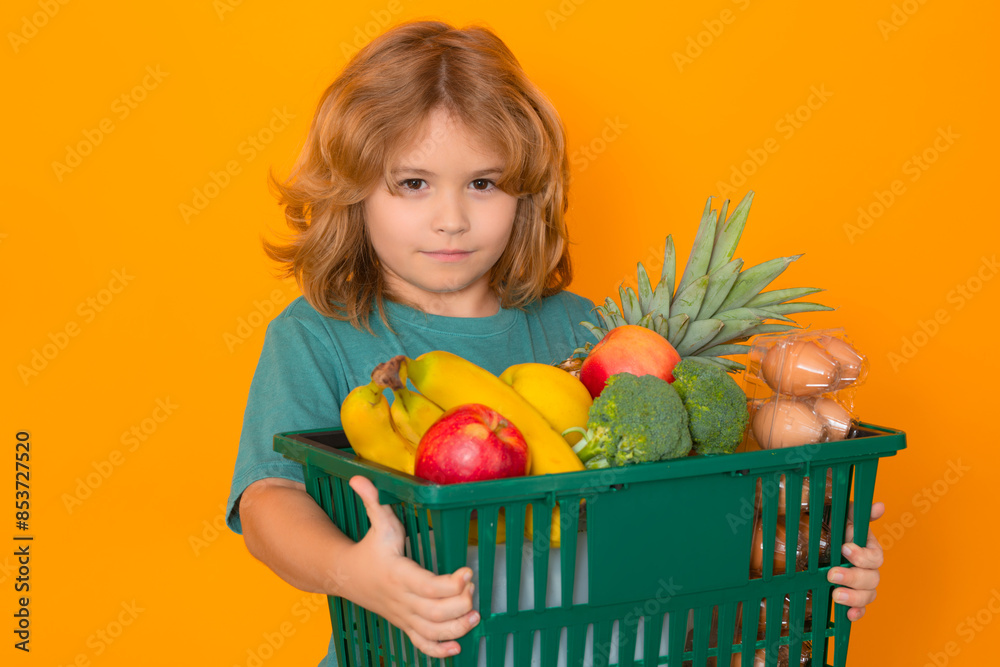 Wall mural Shopping grocery. Kid at vegetable supermarket. Child with shopping basket. Child choosing food in store or grocery store, isolated background, banner.