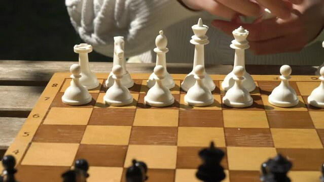 A young adult woman playing chess in the garden of her house or in summer park