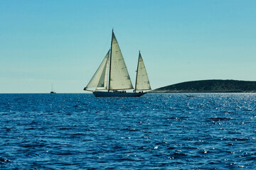 A sailboat is sailing in the ocean with a clear blue sky in the background
