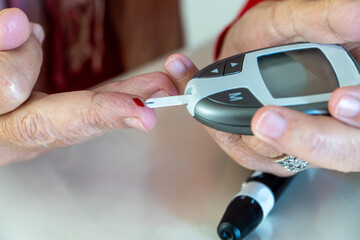 Close up of woman with chronic diabetes testing blood glucose level at home to avoid hypoglycemia