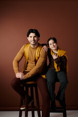 A father and son sit together in a studio setting, smiling and looking happy.