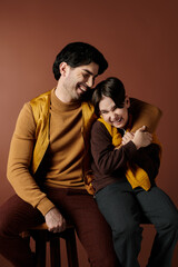 A father and son share a tender moment, laughing together in a studio setting.