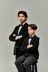 A father and son stand together in matching black suits, arms crossed.