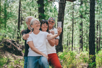 Group of senior friends enjoying a trekking day in the forest, elderly caucasian couples of retirees smiling carefree take selfie with smartphone, healthy lifestyle in outdoors concept