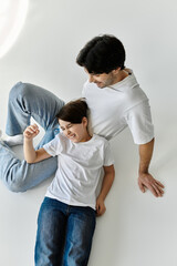 A father and son share a moment of laughter and joy, laying on a white floor.