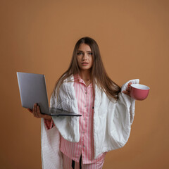 Fototapeta premium Holding laptop, in sleep clothes. Young pretty woman is against background in the studio
