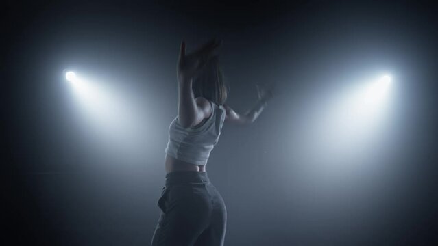 Woman dance in nightclub. Silhouette dancer woman performing dance figures in fog. Young woman dancing in smoky studio. 4K, UHD