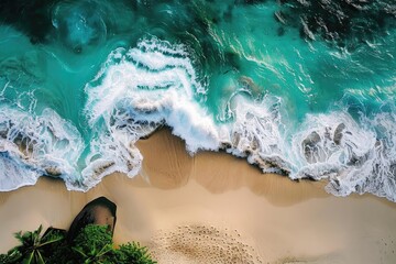 Fototapeta premium Aerial view of turquoise ocean waves crashing onto a sandy beach with lush green foliage, creating a tropical paradise landscape.