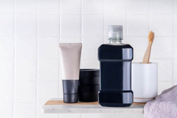 Charcoal Mouthwash, dental oral hygiene rinse aid liquid, trendy alternative detoxifying mouthwash with charcoal with toothbrush, charcoal paste and tablets for cleaning teeth on bath background