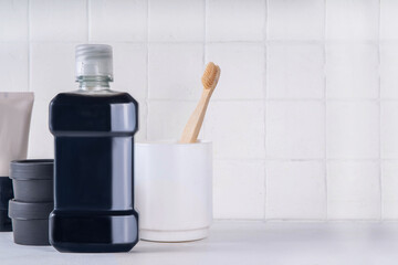 Charcoal Mouthwash, dental oral hygiene rinse aid liquid, trendy alternative detoxifying mouthwash with charcoal with toothbrush, charcoal paste and tablets for cleaning teeth on bath background