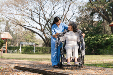 Fototapeta premium Elderly Woman in Wheelchair Assisted by Caregiver in Outdoor Rehabilitation Session in a Park Setting