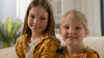 Two happy Caucasian children little girls daughters looking at camera together dental healthy toothy smile sisters kids friends posing relax showing positive emotion family couch living room indoors