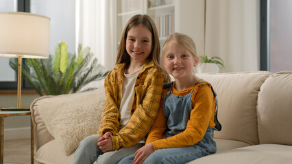 Two happy Caucasian children little girls daughters looking at camera together dental healthy toothy smile sisters kids friends posing relax showing positive emotion family couch living room indoors