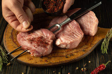 Close-up of butcher hands adding spices to raw pork steaks. Concept of preparing meat for a picnic. European cuisine