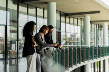 Three people standing on a glass bridge looking at their phone The scene was casual and relaxed as people were unhurried and enjoying their time together.