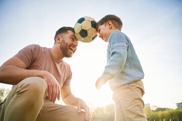 Soccer ball, holding it by heads, fun. Happy father with son are on the field at summertime