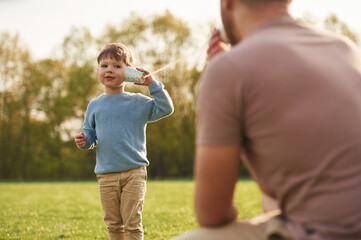 White paper cup telephone. Happy father with son are having fun on the field at summertime