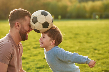Positive emotions, holding soccer ball by heads. Happy father with son are having fun on the field at summertime