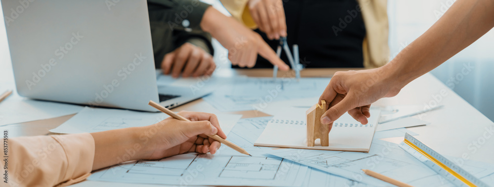 Wall mural Professional architect team discussion about architectural project on meeting table with blueprint and wooden block scatter around at modern office. Closeup. Focus on hand. Delineation.