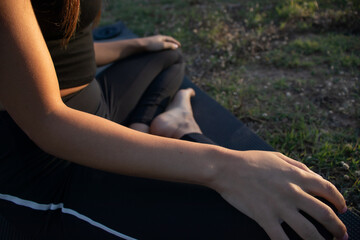 Beautiful young female practicing yoga in nature on a green grass during golden hour in summertime...
