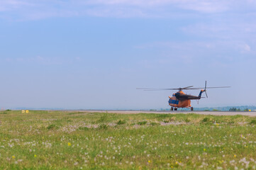 Orange helicopter on a green meadow preparing to take off. Sunny summer day. Foreground blur.