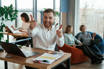 Fototapeta premium Happy man is smiling, sitting by table. People are working in the office with bean bags chairs in it