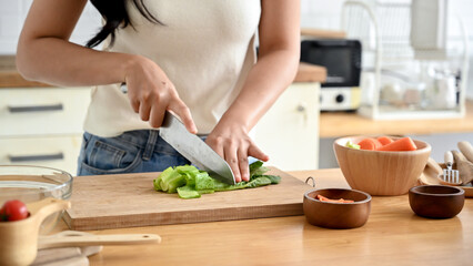 A close-up image of a woman cutting lettuces on a cutting board at a wooden kitchen tabletop, cooking in the kitchen. healthy food, lifestyle, home cooking
