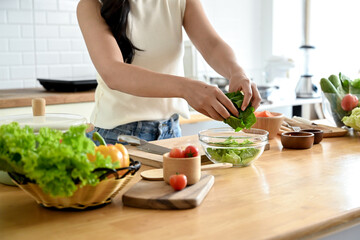 A cropped image of an attractive Asian woman making her healthy salad bowl in the kitchen, putting some lettuces in a bowl. home cooking, healthy and wellness lifestyle, domestic life